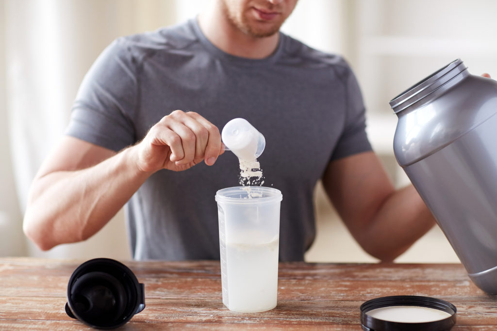 sport, fitness, healthy lifestyle and people concept - close up of man with jar and bottle preparing protein shake