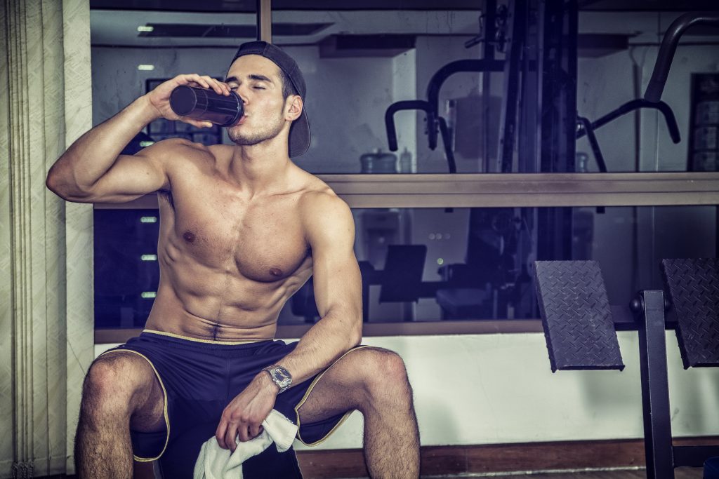 Man in gym drinking a post-workout recovery drink to prevent muscle soreness.