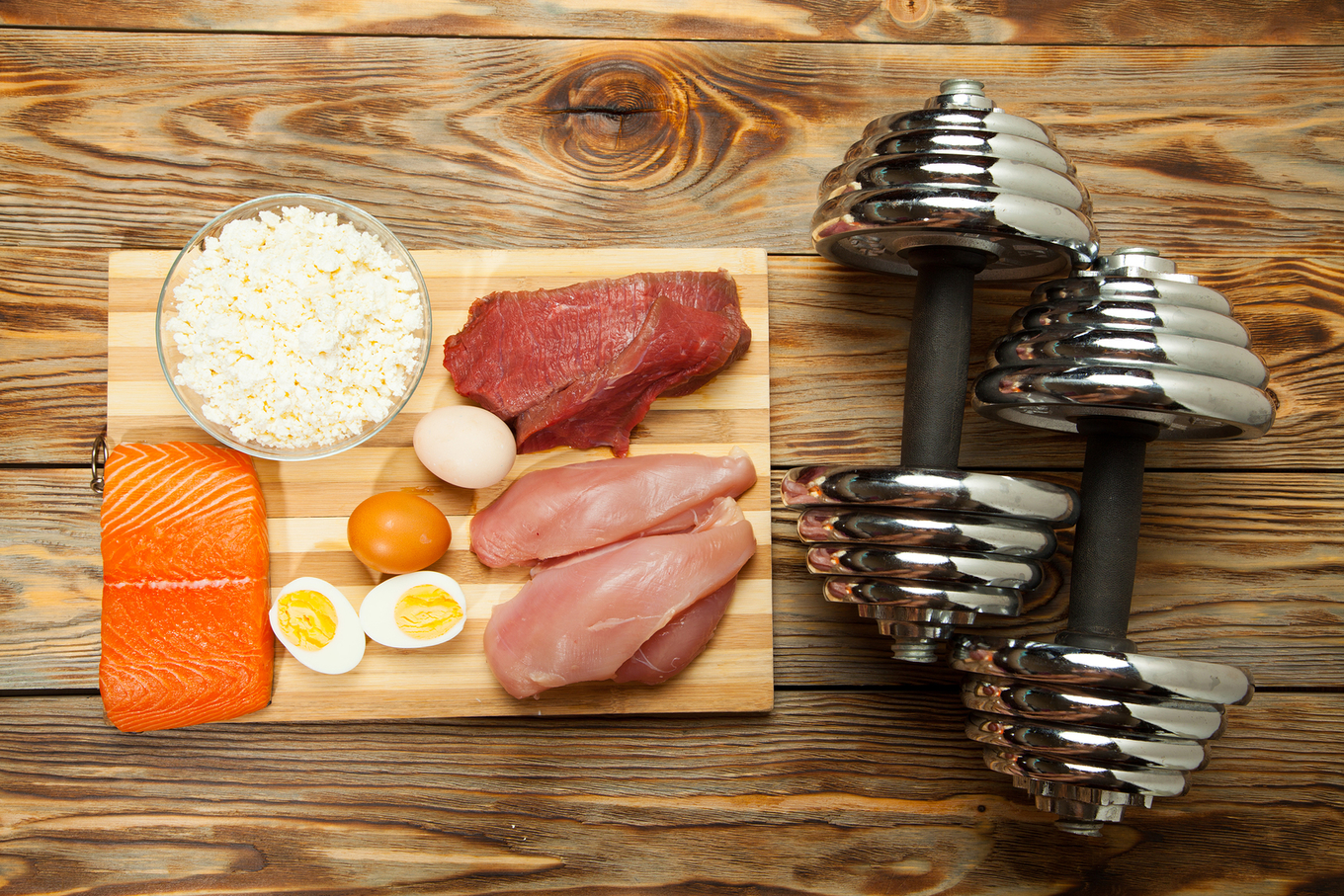 Protein diet, fish, cheese, eggs, meat, chicken and dumbbells on a wooden background